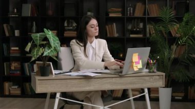 Takım elbiseli genç bir kadın ofis masasında oturur ve yorgun bir şekilde sırt ağrısı çekerek uzanır. Kadın ofiste çok çalışıyor ve kemik ağrısı çekiyor. Bilgisayarın önünde statik çalışma