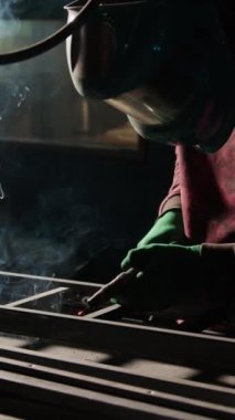 Koruyucu teçhizattaki usta demirci, metal parçaları kaynak makinesiyle birbirine bağlıyor. Endüstriyel atölye çalışanı