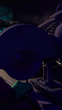 Yetenekli demirci çeliği açı öğütücüsüyle keser ve karanlık atölyede turuncu kıvılcımlar oluşturur. İşçi fabrikada metal profilini testereyle kesti