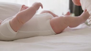 Beyaz bir kıyafetle sırt üstü yatan aktif bebek ellerini ve ayaklarını hareket ettiriyor. Yeni doğan masaj uzmanıyım. Kadın doktor egzersiz ve masaj için bebek derisini nemlendirir.