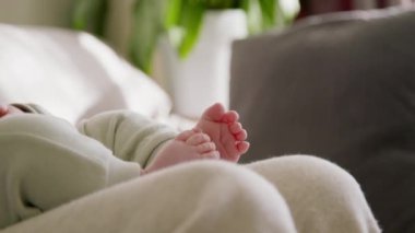 Küçük ayaklı bebeklerin yakın plan görüntüsü. Bebek annesinin kollarında oturuyor ve nazikçe ayaklarıyla oynuyor. Parlak, rahat bir ev. Güzel annelik