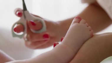 Bebeğin ayak tırnaklarını makasla kesen genç bir annenin yakın çekimi. Evde banyo yaptıktan sonra yeni doğmuş bir bebeğe bakma süreci. Bebekler için özel makas