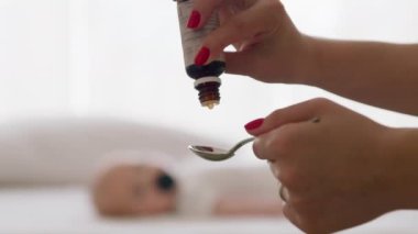 Anne bebekler için antikolik solüsyon damlatıyor. Yeni doğan bebek arka planda bulanıklaştı. Mide ağrısı, kolik, şişkinlik, kramplar ve rahatsızlık için çözümler. Bebeğin mide ağrıları için hazırlık.