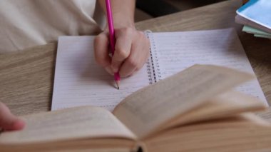 Bir kız öğrencinin, bir kitaptaki bilgileri okuyup özetlediği ve kağıda not aldığı yakın plan görüntüsü. Solak kız kitaptaki bazı fikirleri gözden geçiriyor ve bir deftere yazıyor.