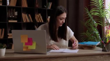 Esmer öğrenci iş arkadaşlarıyla bir grup projesi hazırlıyor. Genç kadın bilgisayardaki meslektaşlarıyla video görüşmesi yapıyor ve projeyi tartışıyor. Öğrenci not alıyor.