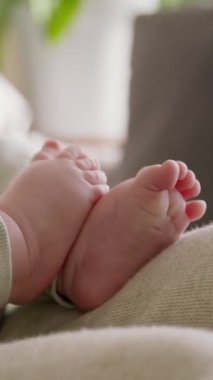 Annesinin kollarında yatarken, yenidoğan ayaklarına ve ellerine yakın plan. Bebek tek başına ayaklarıyla oynuyor, cildi yumuşak ve kadife gibi. Huzurlu, huzurlu ve rahat bir ortam.