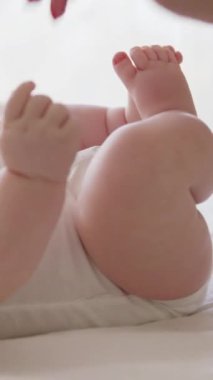 Genç annenin parmaklarıyla oynadığı ve sırtında küçük bir bebekle oynadığı yakın plan bir görüntü. Annem bebek bakıcılığı yapıyor ve onu mutlu ediyor. Beyaz elbiseli çocuk annesiyle aktif olarak etkileşimde.