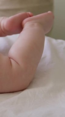 Karnının üzerinde uzanan yumuşak ve açık tenli bebek bacaklarını tekmeliyor. Küçük bir çocuğun dibi. İyice sulandırılmış bebek teni. Sağlık ve cilt bakımı, bebek gelişimi kavramı.