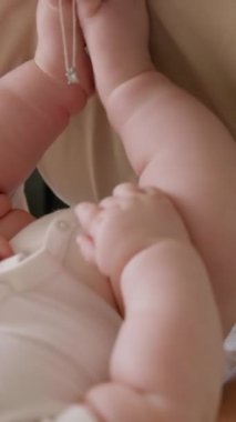 Annesiyle oynayan beyaz elbiseli bir bebeğin yakın çekimi. Aktif çocuk bacaklarını annesinin boynuna kaldırıyor. Sağlıklı ve aktif bir bebekle hoş aile anları. Hoş annelik.