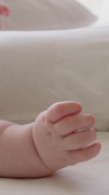 Parlak bir odada sırtüstü uzanmış beyaz elbiseli bir çocuğun yan görüntüsü. Lateks emziği. Aktif bebek bacaklarını ve ellerini tekmeliyor. Pürüzsüz, temiz, açık tenli bebek