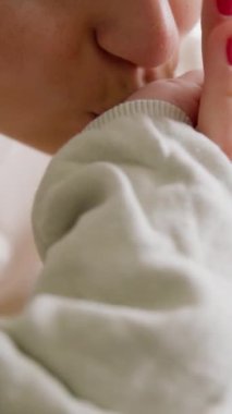 Annenin bebeğe nazikçe konuşmasının, küçük ellerini tutmasının ve onları usulca öpmesinin yakın çekimi. Gülümseyen ve sevecen bir anne yeni doğan çocuğuna bakıyor. Annelik kavramı. Anne doğum izninin tadını çıkarıyor.