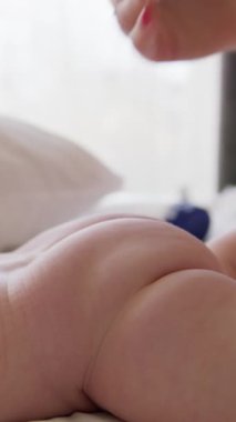 Annenin yeni doğan bebeğinin poposuna krem sürerken ve nazikçe masaj yaparken yakın plan görüntüsü. Bebek karnının üstünde yatıyor. Kadın banyodan sonra bebek derisini nemlendiriyor. Rutin atmosfer
