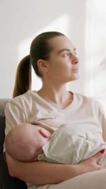 Genç anne kanepede oturup yeni doğmuş bebeğini kollarında emziriyor, şefkatin tadını çıkarıyor, koşulsuz sevgiyi hissediyor. Emzirme, çocuk sağlığı, doğal beslenme konsepti.