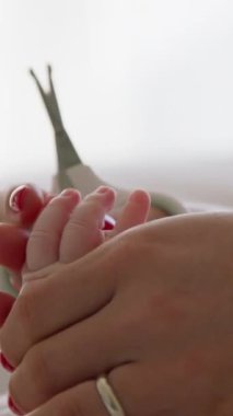 Genç bir annenin elleri bebek tırnaklarını makasla kesiyor. Evde banyo yaptıktan sonra yeni doğmuş bir bebeğe bakma süreci. Bebekler için özel makas