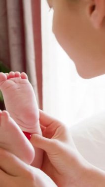 Güneşli bir sabah genç annesi yeni doğmuş bebeğini seviyor. Bir annenin bebek ayaklarının tabanını nazikçe öperkenki görüntüsü. Kadın bebek bakımı rutinini yapıyor ve bebek ayaklarıyla oynuyor.