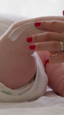 Genç bir annenin elleri, yeni doğan ayaklarına bol miktarda krem sürüp nazikçe masaj yapıyor. Kadın ayaklarının derisini doğal bebek ürünleriyle nemlendiriyor..
