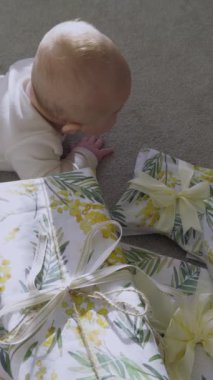 Asyalı bebek halıda yüzüstü yatıyor ve ellerini ve ayaklarını sallıyor. Küçük çocuk güzel paketlenmiş hediye kutularının yanında. Aile tatili kavramı