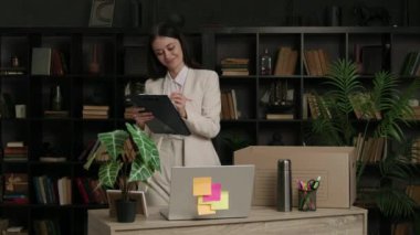 Mutlu kadın kişisel eşyalarını toplayıp karton bir kutuya koyar. Neşeli iş kadını, başka bir ofise nakledilmek üzere kutuya koyduğu şeyleri bir kağıt parçasına işaretler..