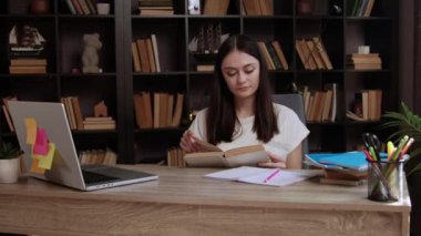 Rahat gülümseyen esmer kız eski bir kitaptan bir roman okuyor. Modern bir odada, arkasında bir kitaplık olan bir ofis masasında kız derslerini okula hazırlıyor.