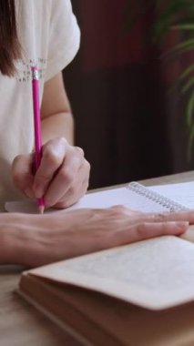 Ofis masasında ders hazırlayan esmer bir öğrencinin yakın plan görüntüsü. Kız eski bir kitaptan okuyor ve ders çalışıyor ve not defterindeki bir kalemle not alıyor. Genç kadın evde okuyor.