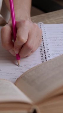 Bir kız öğrencinin, bir kitaptaki bilgileri okuyup özetlediği ve kağıda not aldığı yakın plan görüntüsü. Solak kız kitaptaki bazı fikirleri gözden geçiriyor ve bir deftere yazıyor.