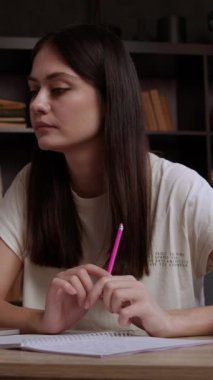 Tedbirli bir gülümsemeyle üniversite için proje hazırlayan esmer bir öğrencinin yan görünüm portresi. Öğrenci internetten bir not defterine bilgi yazar. Genç kadın notları.