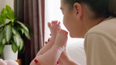 Kişisel hijyenini yaparken bir bebeğin çıplak ayaklarıyla annenin yüzüne dokunması. Genç anne, yeni doğmuş bebeklerle evdeki parlak bir odada sevgiyle oynuyor.