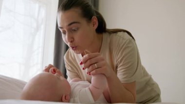 Genç ve etkileyici esmer anne, sırt üstü yatan bebeğini neşelendiriyor. Mutlu genç kadın yeni doğmuş bebeğiyle oynuyor, burnunu bebek burnuna değdiriyor. Mutlu annelik