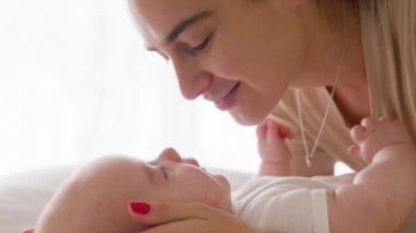 Yeni doğmuş bebeğiyle oynayan neşeli ve mutlu bir annenin yakın çekimi. Güzel anne, sırtüstü yatıp sevgiyle oynayan aktif bebeğin burnuna dokunur.