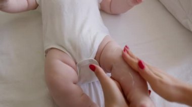Bebeğin ayaklarını kremle nemlendirirken bir annenin elinin yakın plan görüntüsü. Kırmızı manikürlü genç anne banyodan sonra bebek bakımını yapıyor. Yeni doğan bakım konsepti