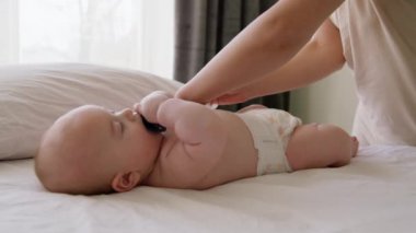 Ağzında bir emzik ile sırt üstü uzanmış rahat bir bebek. Genç anne bebeğe çevre dostu temiz bir bez takıyor. Bebeği evde yıkadıktan sonra hijyen ve bakım rutini..