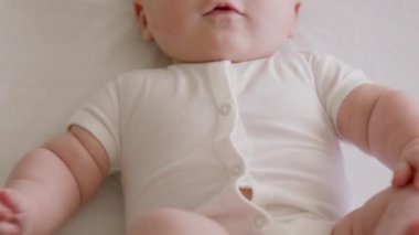 Gülümseyen neşeli ve aktif bir bebeğin yakın plan görüntüsü. Beyaz elbiseli bebek mutlu bir şekilde gülümser ve kollarını aktif olarak sallar ve çıplak bacaklarını kaldırır. Yeni doğmuş bir bebeğin masum gülümsemesi.