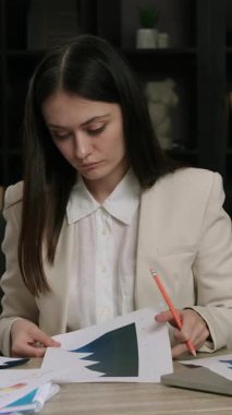 Klasik takım elbiseli ciddi bir kadın bir ofis masasında oturup müşteri şirketlerinin geliştirme istatistiklerini analiz eder. İş geliştirme şirketi. Bir sürü yeşil çiçekli modern ofis.
