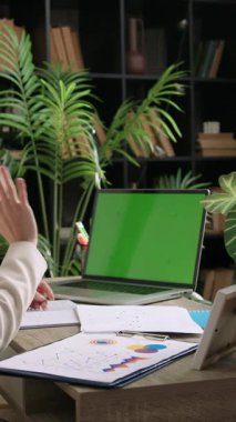 İş kadını, iş yerindeki online toplantıda el sallıyor. Kadın proje hazırlığı için kağıtları alır
