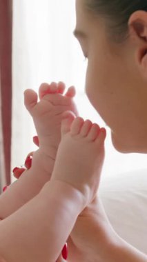 Kişisel hijyenini yaparken bir bebeğin çıplak ayaklarıyla annenin yüzüne dokunması. Genç anne, yeni doğmuş bebeklerle evdeki parlak bir odada sevgiyle oynuyor.