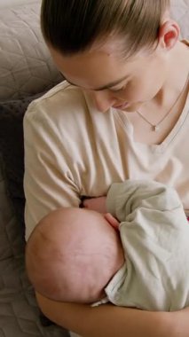 Genç anne kanepeye oturup bebeğini emziriyor. Kadın aktif ve sağlıklı bebeğini anne sütüyle besliyor. Kadınlar evlerinde emzirme sürecinden zevk alırlar.