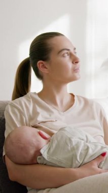 Genç ve güzel anne sessizce bebeğini anne sütüyle emziriyor. Mutlu kadın, bebeğini emzirirken sevgiyle gülümsüyor ve ona bakıyor. Sevgi vahasında evde emzirmek çok keyifli.