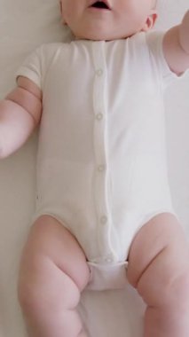 Yukarıda, detaylıca, beyaz bir vücut giysisiyle sırt üstü yatan bir bebek hayal edin. Sağlıklı bir bebeğin tombul küçük bacakları ve elleri aktif olarak sallıyor ve ağzına koyuyor. Yumuşak ve narin cilt