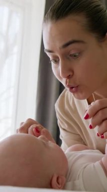 Genç ve etkileyici esmer anne, sırt üstü yatan bebeğini neşelendiriyor. Mutlu genç kadın yeni doğmuş bebeğiyle oynuyor, burnunu bebek burnuna değdiriyor. Mutlu annelik