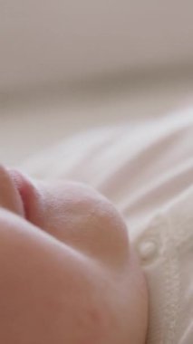 Sırtında yumuşak bir ten olan bir bebeğin yüzü ve gülümsemesi. Kollarını ve bacaklarını hareket ettiren mutlu ve aktif bir çocuğun yan görüntüsü. Neşeli beyaz bir vücut giysisi içinde yeni doğmuş bir bebeğin yakın plan görüntüsü