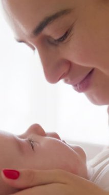 Yeni doğmuş bebeğiyle oynayan neşeli ve mutlu bir annenin yakın çekimi. Güzel anne, sırtüstü yatıp sevgiyle oynayan aktif bebeğin burnuna dokunur.