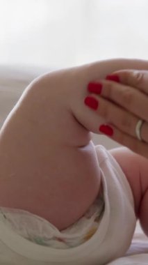 Sırtüstü uzanmış, rahatlamış ve ayaklarıyla oynayan bir bebeğin yakın plan görüntüsü. Bebek bakımı rutinini yapan bir annenin elleri. Anne, aşırı su içmesi için bebeğin ayaklarına krem sürer..