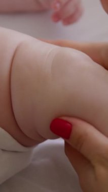 Sırtüstü uzanmış, rahatlamış ve ayaklarıyla oynayan bir bebeğin yakın plan görüntüsü. Bebek ayaklarına kremle masaj yapan bir kadının elleri. Uzman bir masaj yapan bebeğin elleri..
