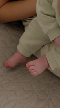 Bebeğin ayaklarını açarken ve annesinin kollarında otururken onlarla oynarken. Bebek elleriyle ve ayaklarıyla tek başına oynuyor. Sessiz ve rahat ev ortamı