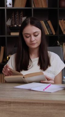 Rahat gülümseyen esmer kız eski bir kitaptan bir roman okuyor. Modern bir odada, arkasında bir kitaplık olan bir ofis masasında kız derslerini okula hazırlıyor.