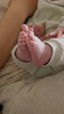 Annesinin kollarında çıplak ayaklı bir bebek, küçük ayakları ve elleriyle coşkuyla oynuyor. Küçük çocuk küçük ellerini ve ayaklarını keşfeder ve onları sevinçle sallar. Sıcak atmosfer