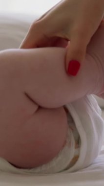 Beyaz tulumlu küçük bebek sırt üstü yatıyor. Anne elleri nemlendirici krem sürerken ve bebeklerin kuru cildine nazikçe masaj yaparken. Genç anne yeni doğan bebeğin sağlığıyla ilgilenir.