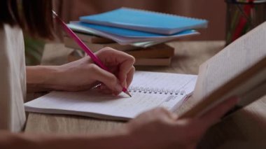Not defterindeki kalemle not alan ve yazan genç bir kadının yakın plan görüntüsü. Öğrenci kavramı, öğrenciler, çalışmalar, sınavlar, sınavlar, öğrenme. Kitaplı ofis masası