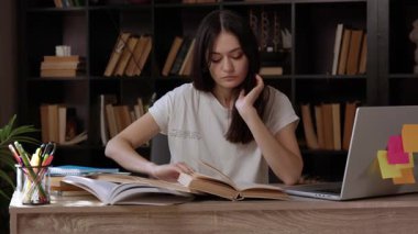 Yorgun genç öğrenci kütüphanede kitap okuyor ve yorgunluktan kafası masanın üzerinde uyuyakalıyor. Modern bir kütüphanedeki kız öğrenci kitap ve bilgisayardan bilgi arıyor