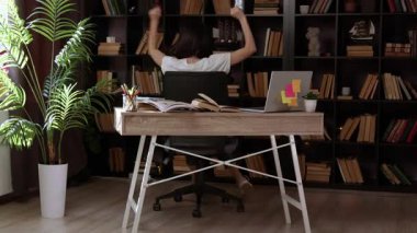 Mutlu genç kadın ofis sandalyesinde dönüyor ve karmaşık bir projeyi bitirmeyi başardığı için mutlulukla dans ediyor. Esmer kız modern bir ofiste bilgisayar eğitimi görüyor.